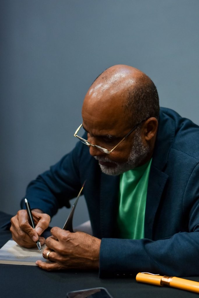 Pr. Raimundo Nascimento escrevendo dedicatória no lançamento do seu primeiro livro